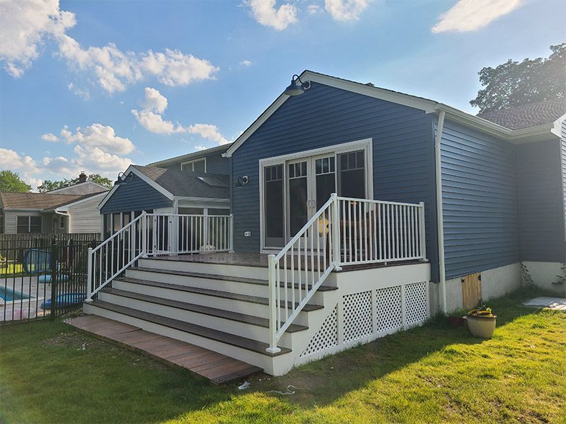 A blue house with a white deck and stairs in front of it.