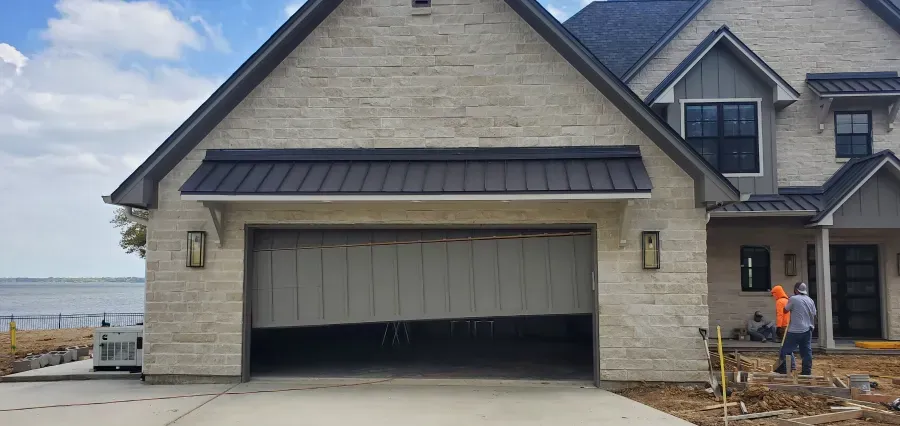 A man is standing in front of a house with a garage door open.