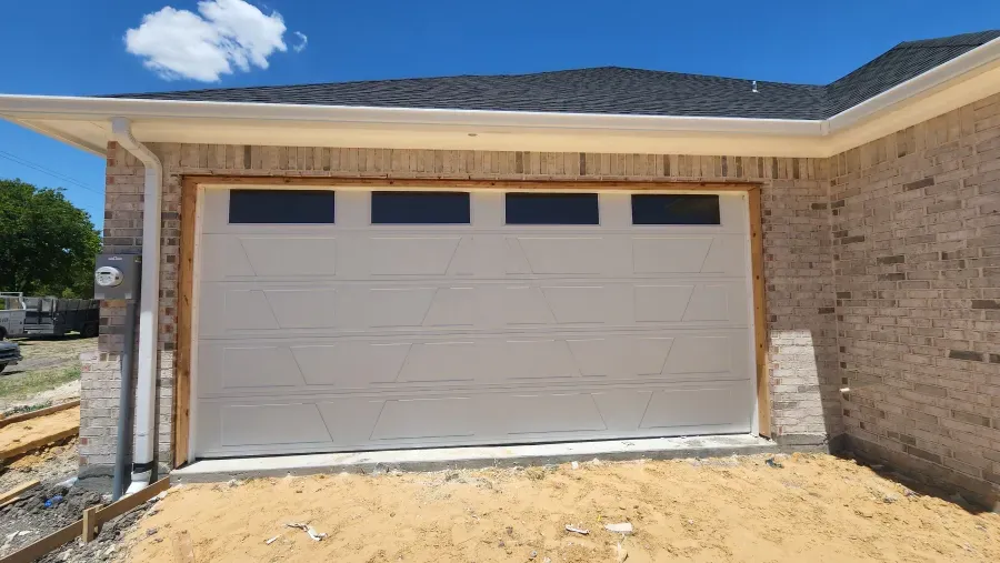 A white garage door is sitting in front of a brick house.