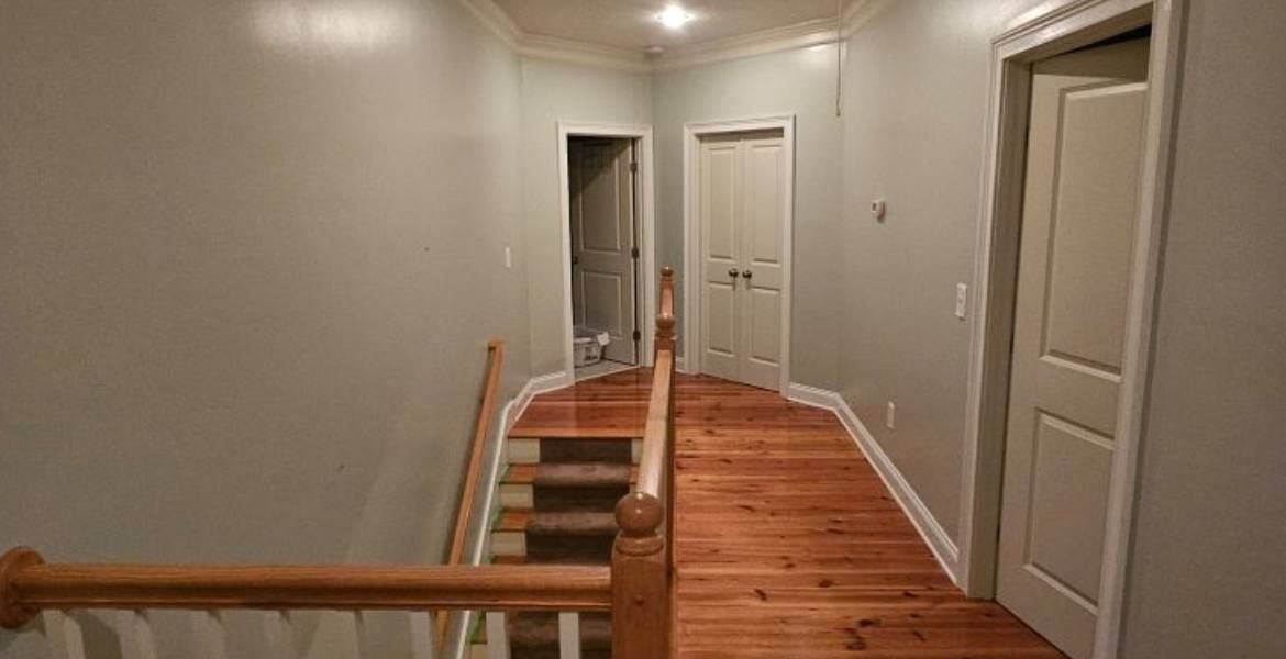 A hallway with wooden floors and stairs in a house.