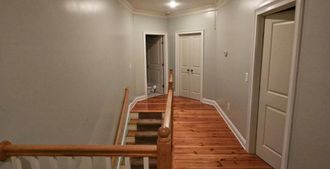 A hallway with wooden floors and stairs in a house.