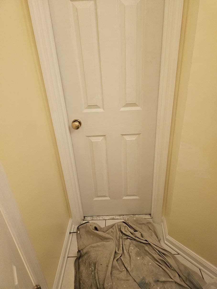 A white door is sitting in a hallway next to a tiled floor.