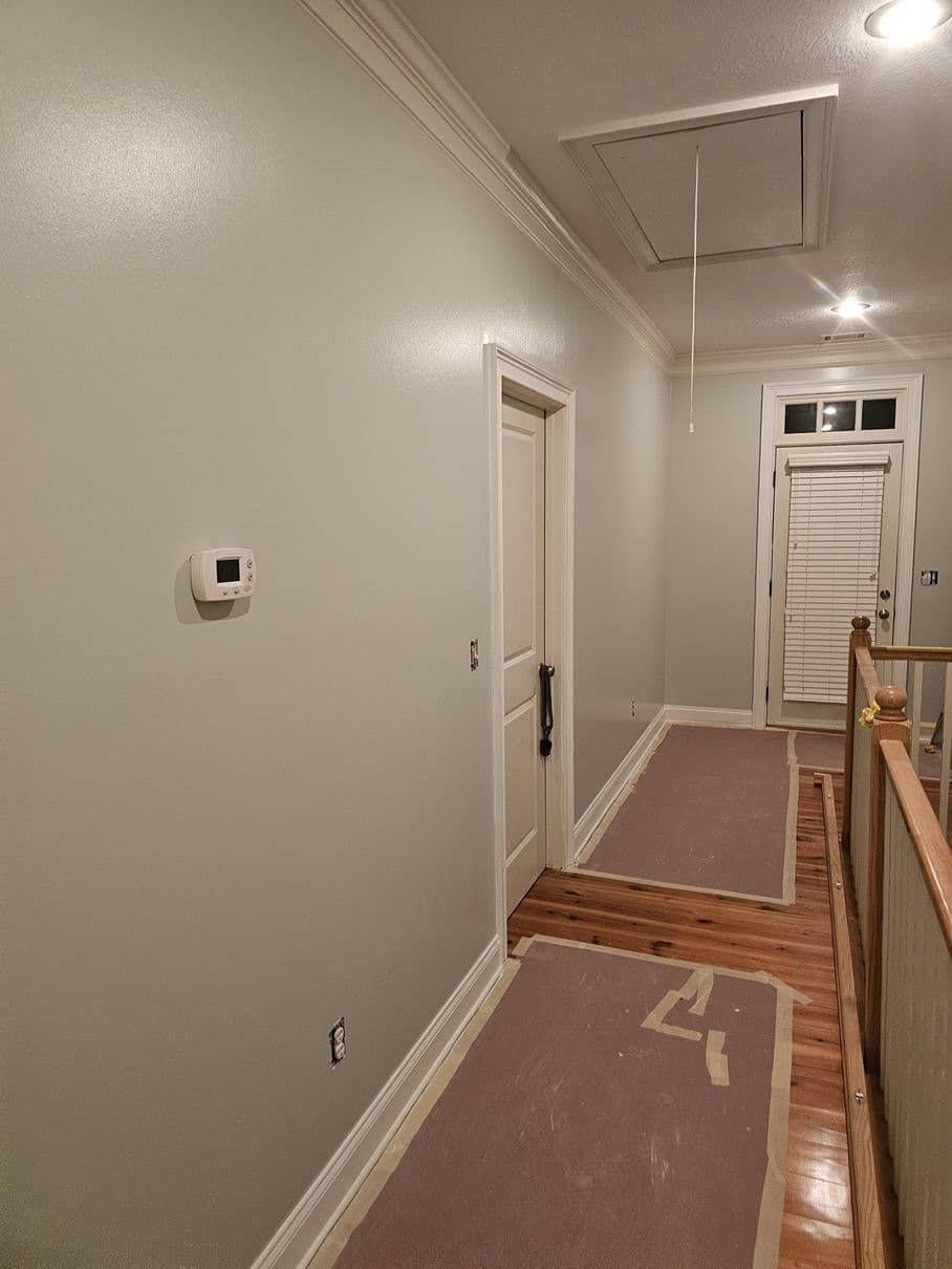 A hallway with white walls and wooden floors is being painted.