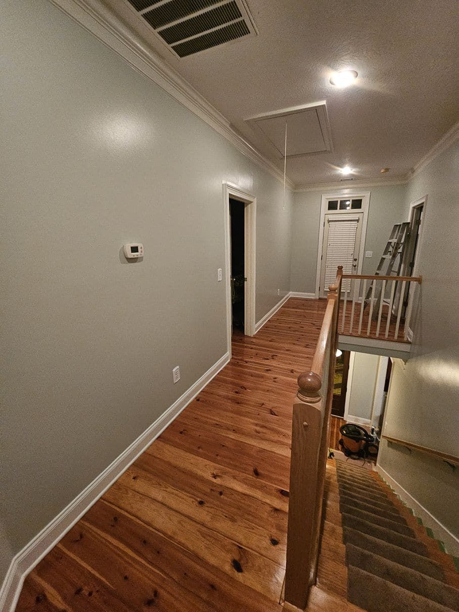 A hallway with wooden floors and stairs in a house.