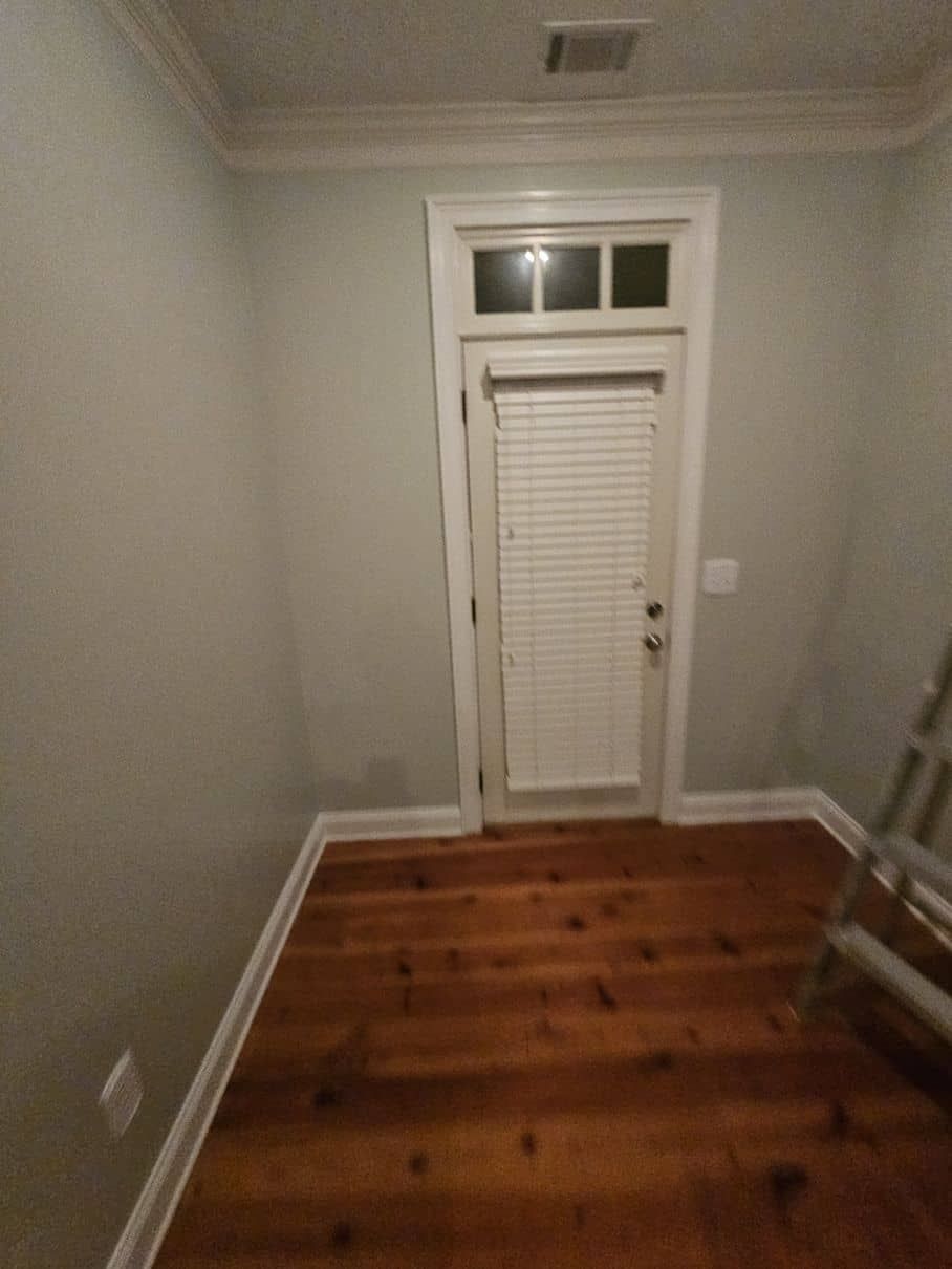 An empty room with wooden floors and a door with blinds.