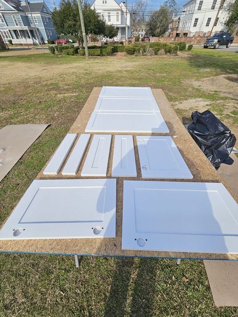 A bunch of white cabinet doors are sitting on top of a table in a grassy field.