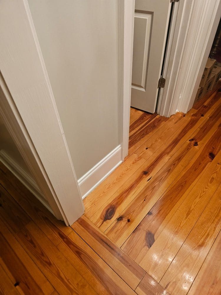 A wooden floor in a hallway next to a door.