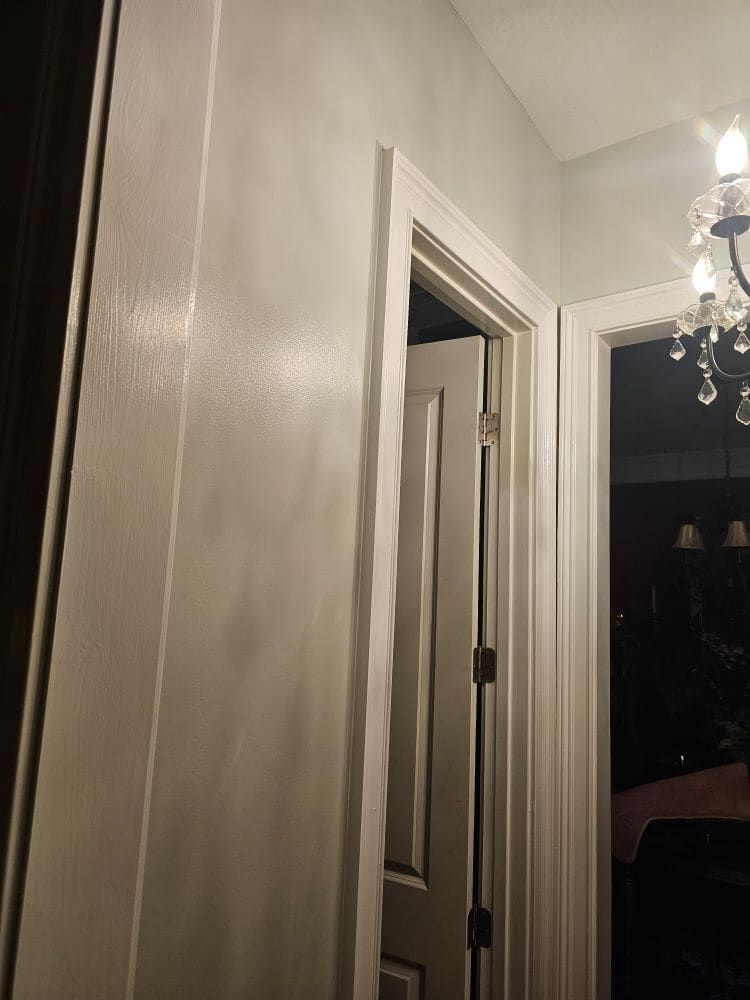 A door is open in a hallway with a chandelier hanging from the ceiling.