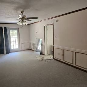 An empty living room with a ceiling fan and a mirror.