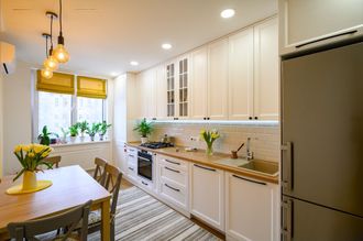A kitchen with white cabinets , a table , chairs and a refrigerator.