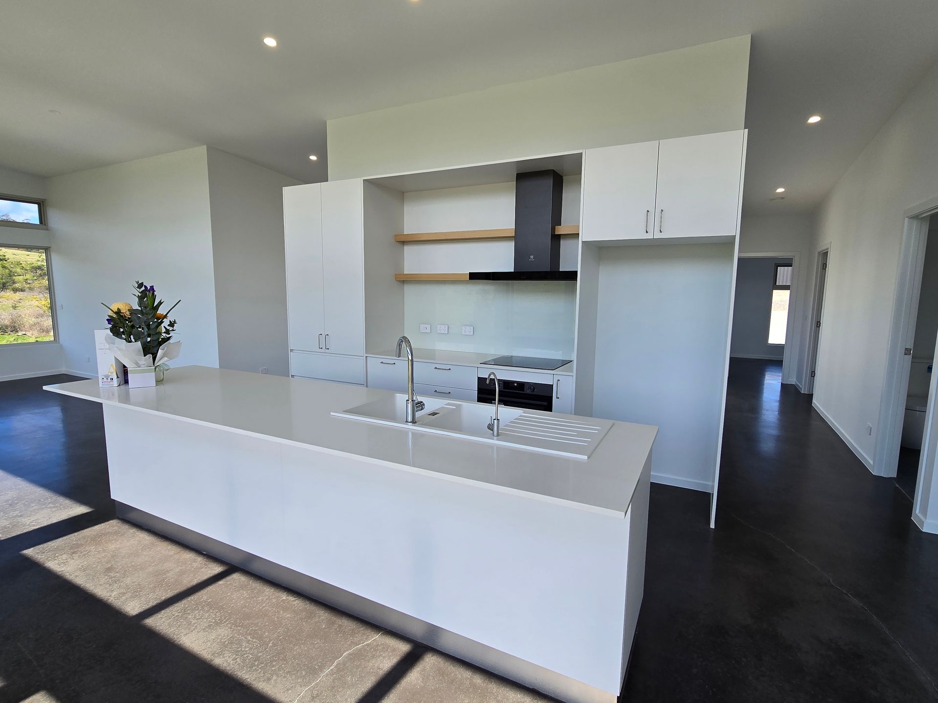 Modern white kitchen with an island, sink, stovetop, and upper cabinets.