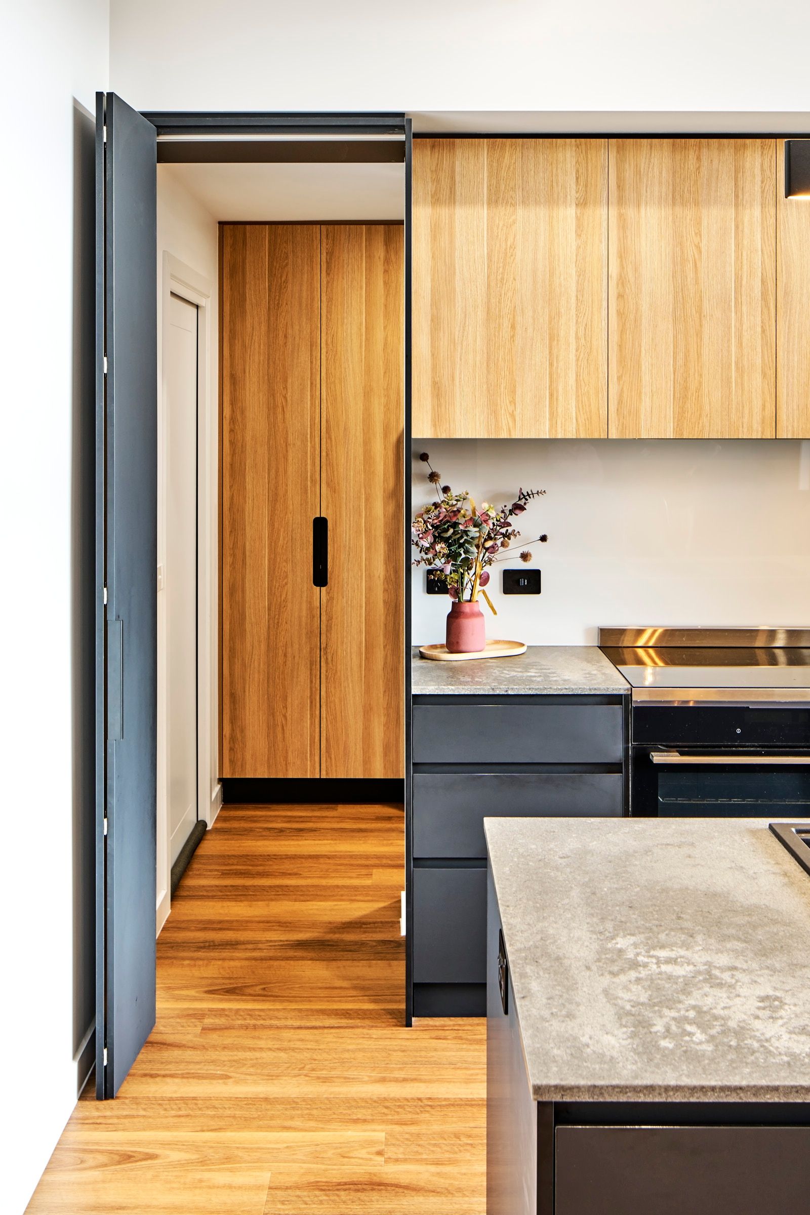 Modern kitchen with wooden cabinets, gray countertops, and a doorway with a partially open blue door.