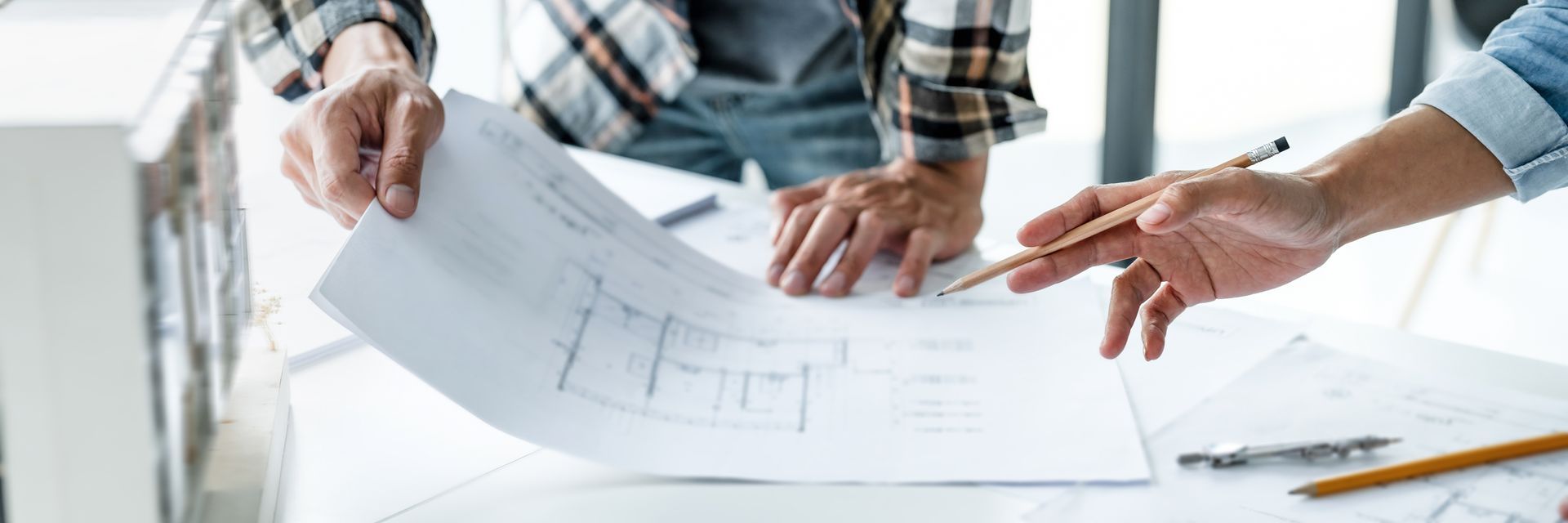 Hands reviewing architectural blueprints on a desk with pencils and tools.