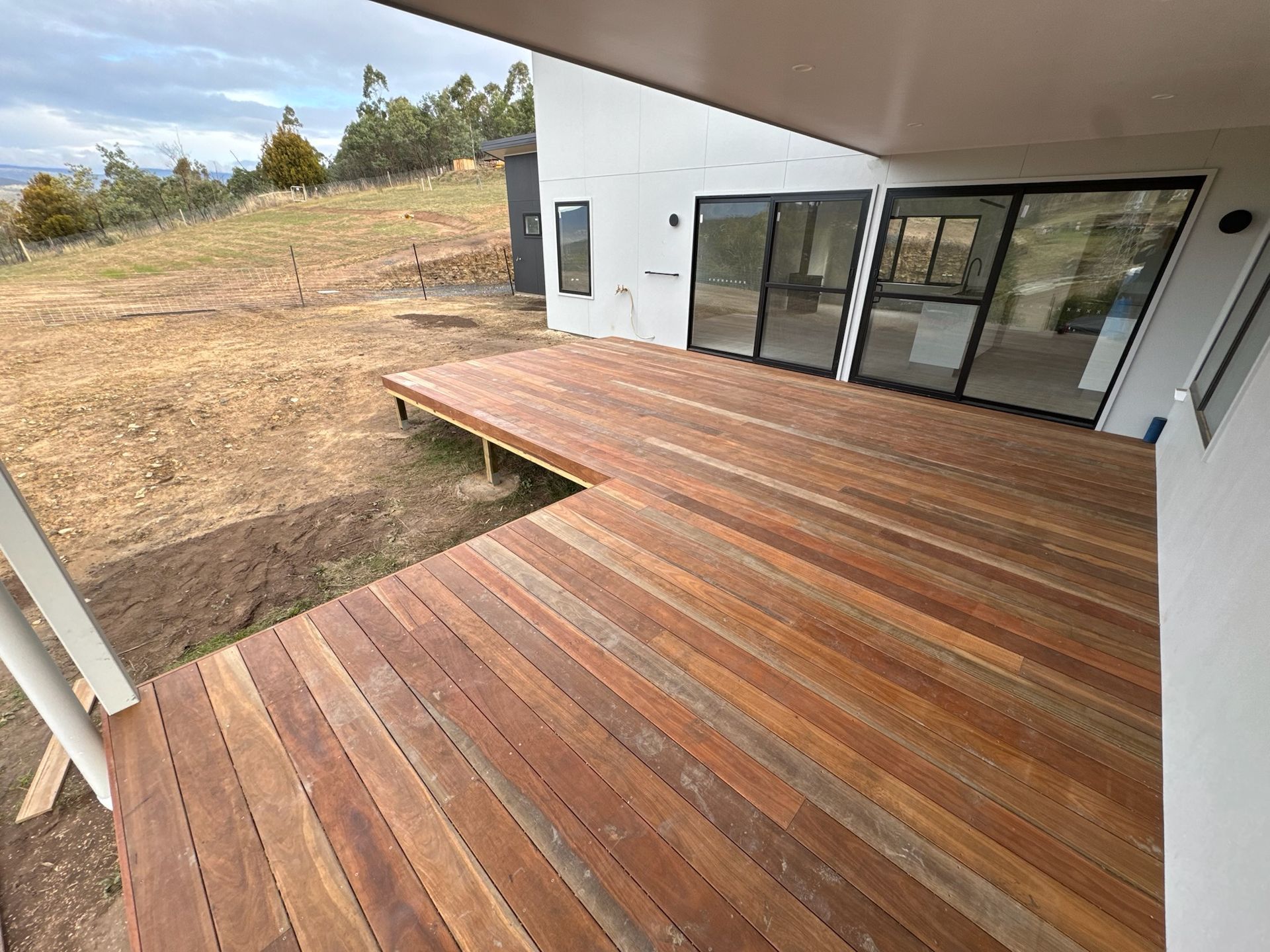 Wooden deck extending from a white house with sliding glass doors.