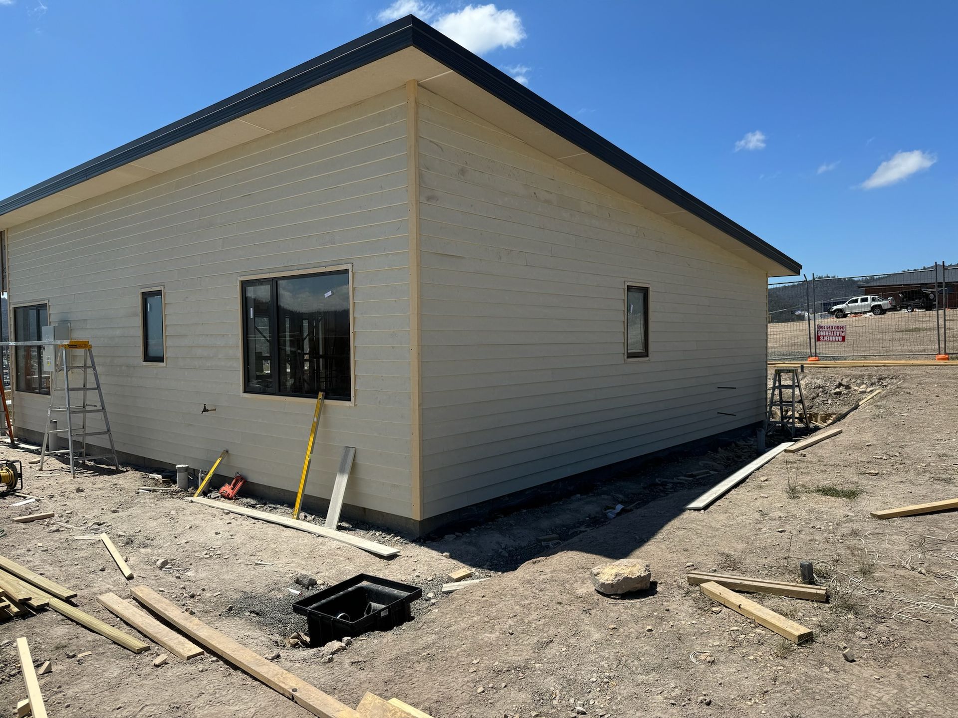 Construction site view of a tan-sided, one-story building with black trim and windows.
