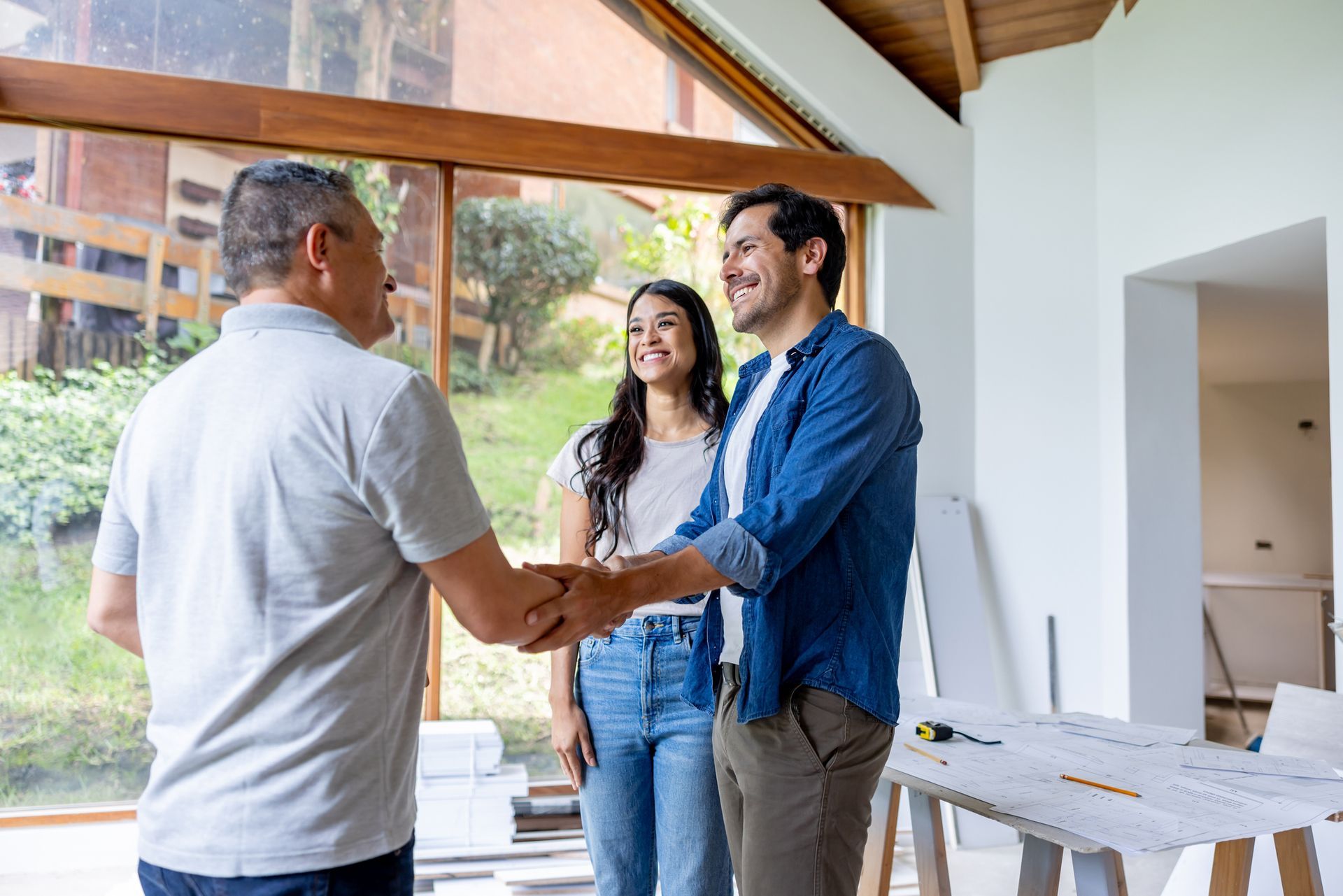 Happy couple greeting the contractor helping design their house with a handshake.