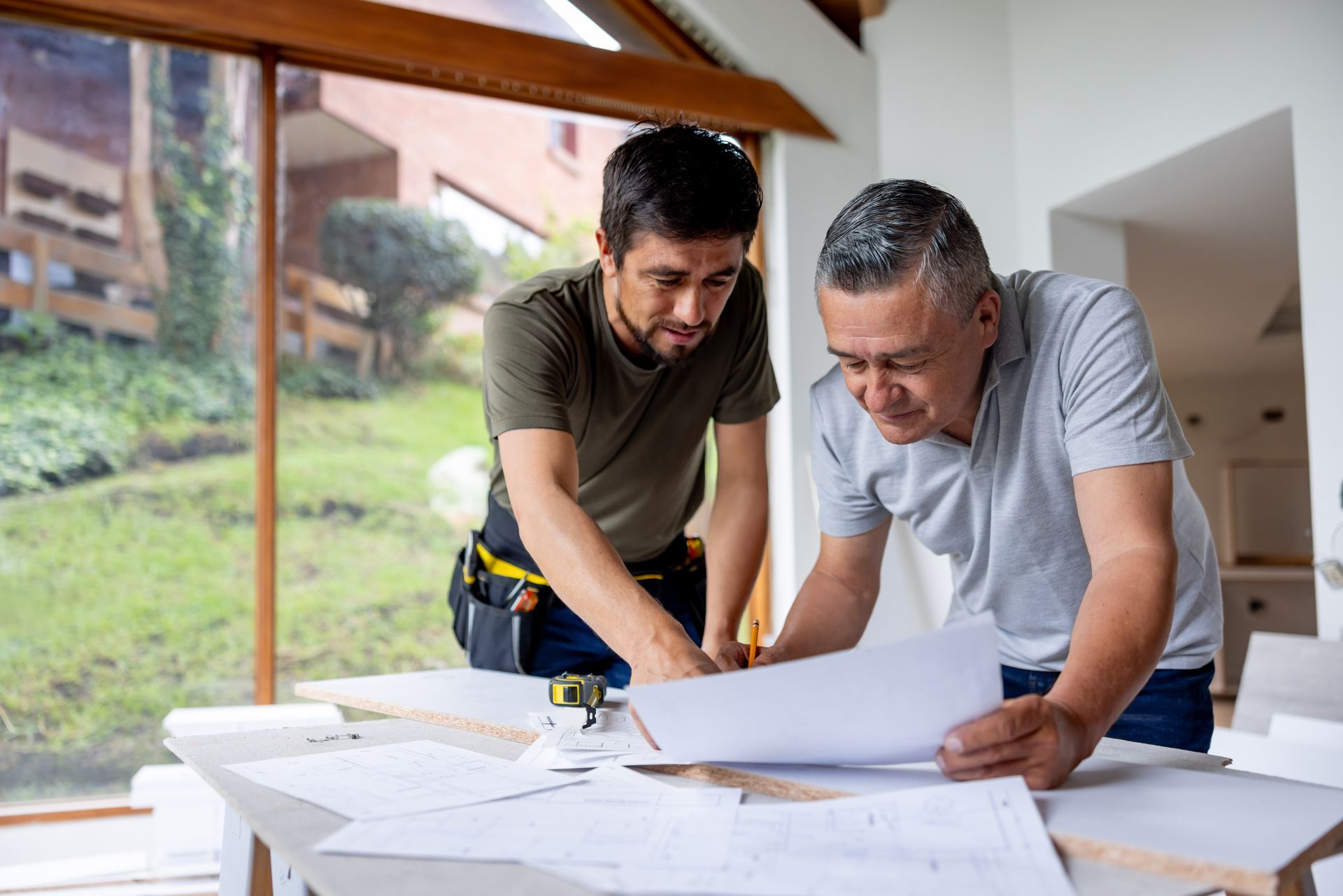 An architect and a building contractor are looking at blueprints while remodelling a house.