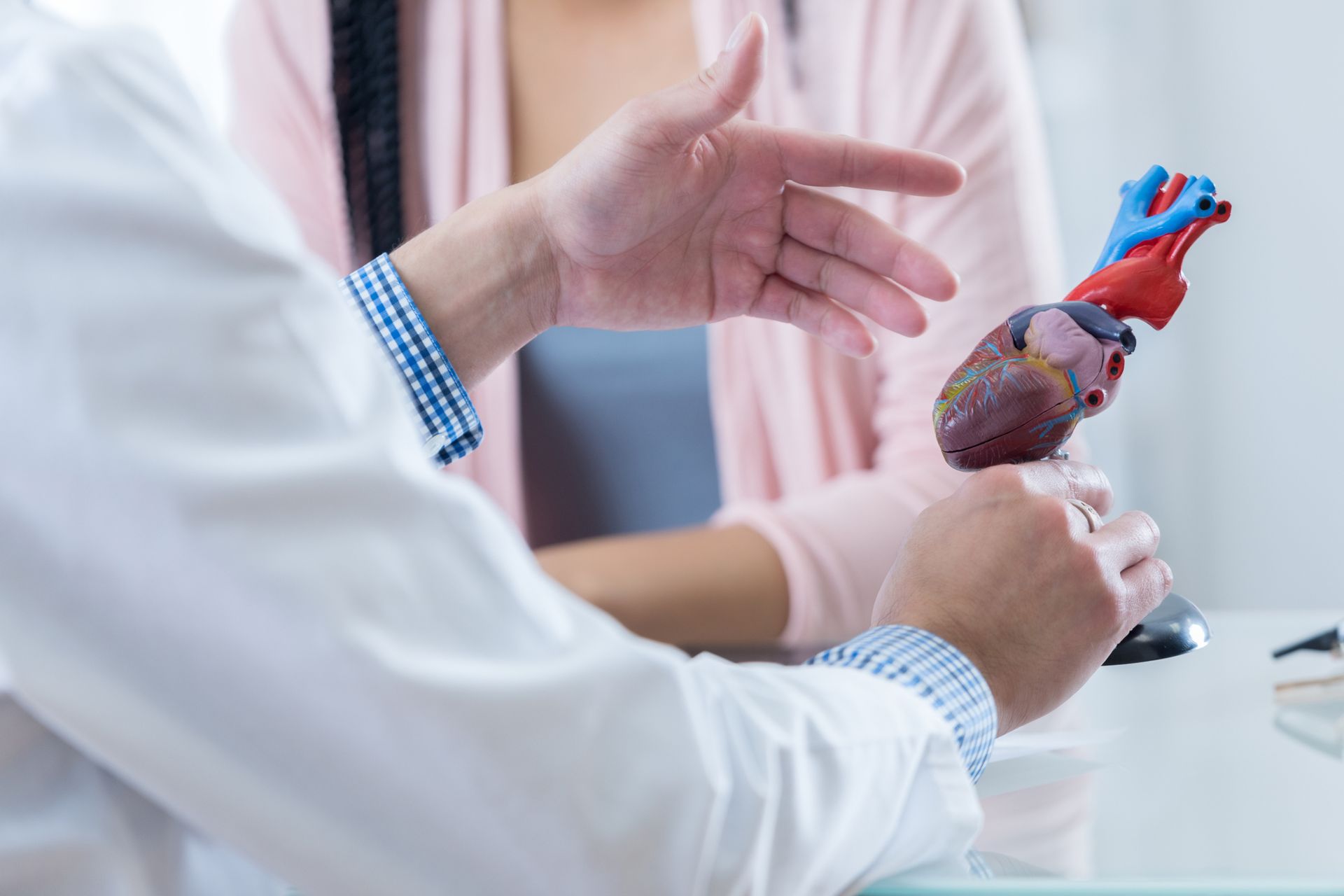 A male cardiologist gestures while discussing diagnosis with an unrecognizable female patient.