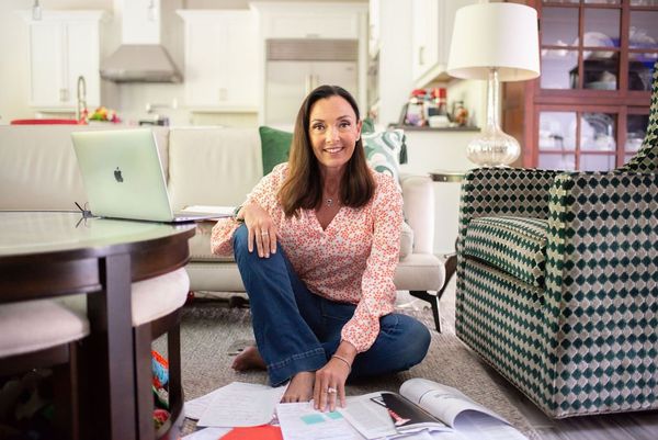 A woman is sitting on the floor in a living room with a laptop.