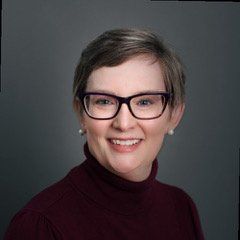 A woman wearing glasses and a turtleneck is smiling for the camera.