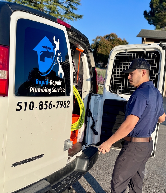 Plumber in blue uniform standing by open white service van with “Rapid Repair Plumbing” logo and phone number.
