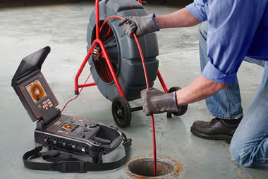 Worker using a drain inspection camera to inspect a floor drain beside open equipment case