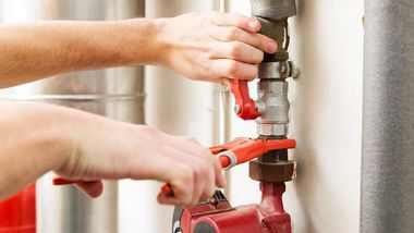 Hands tightening a red pipe valve with a wrench in a utility room