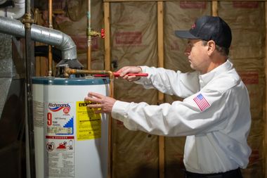Technician checking a water heater with a wrench in a basement utility room
