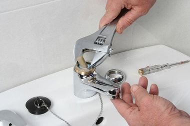 Hands using a wrench to tighten a chrome bathroom faucet on a sink