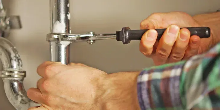 Hands using a wrench to tighten a pipe fitting under a sink.