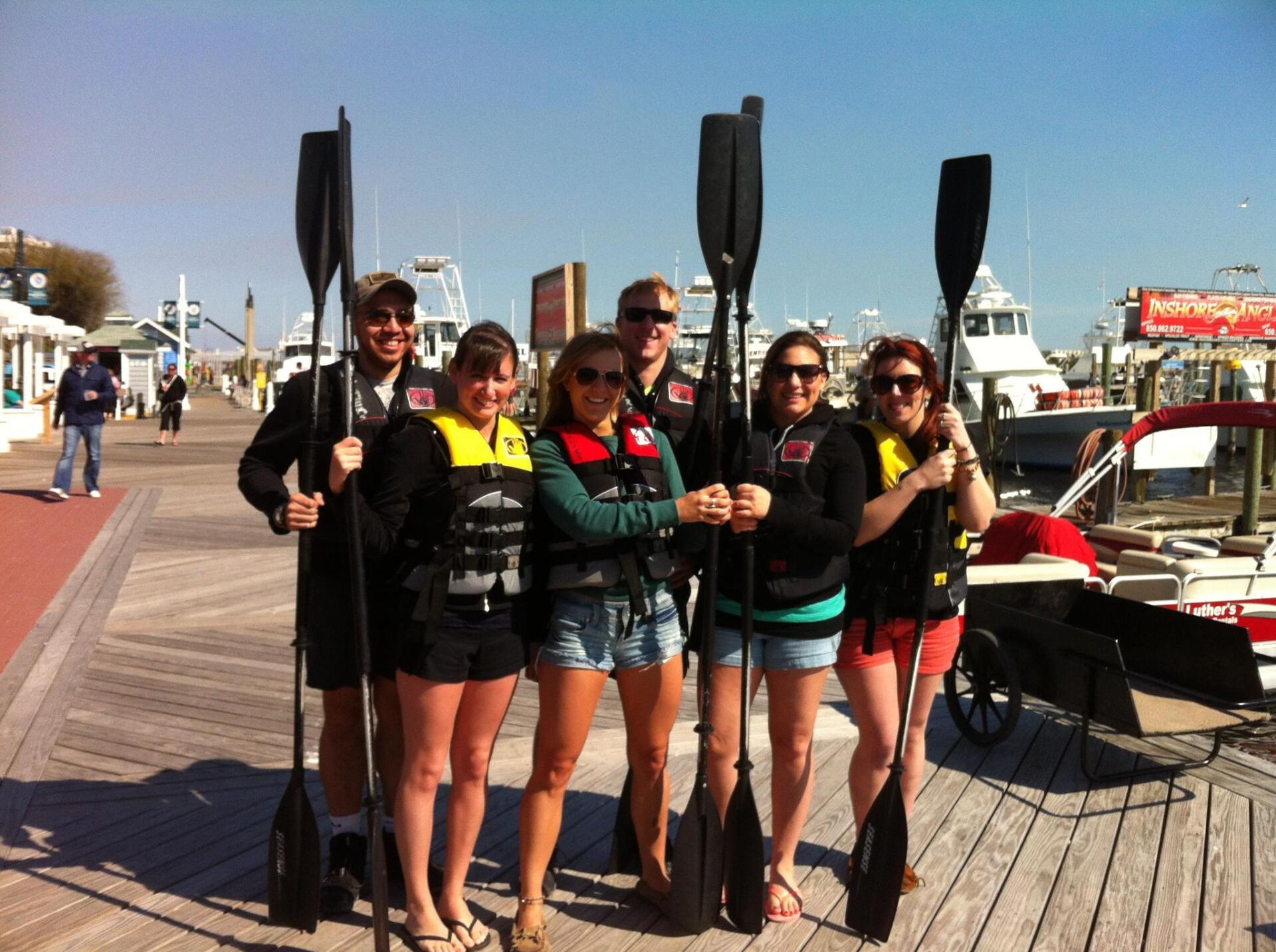 4 females & 2 males holding kayak paddles