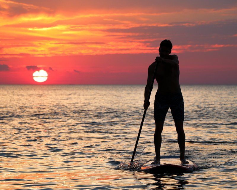 Person on a stand-up paddle board while sun sets over the ocean
