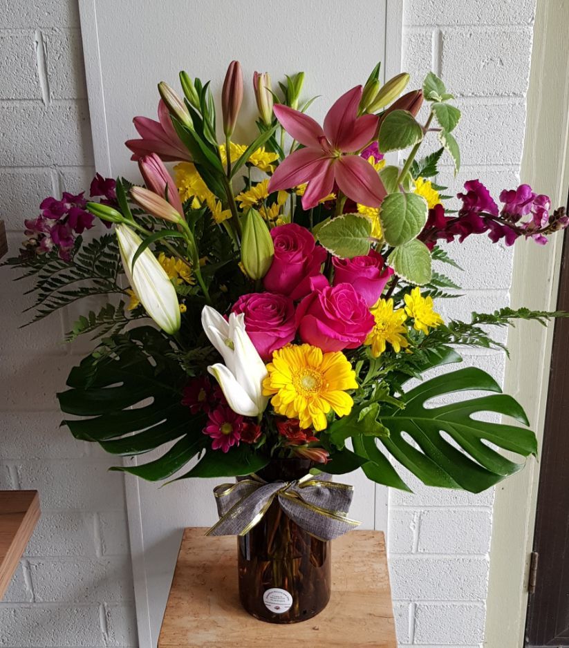 A Vase Filled With Flowers is Sitting on a Wooden Shelf — Greenfield Blooms and Gifts In Wanguri, NT