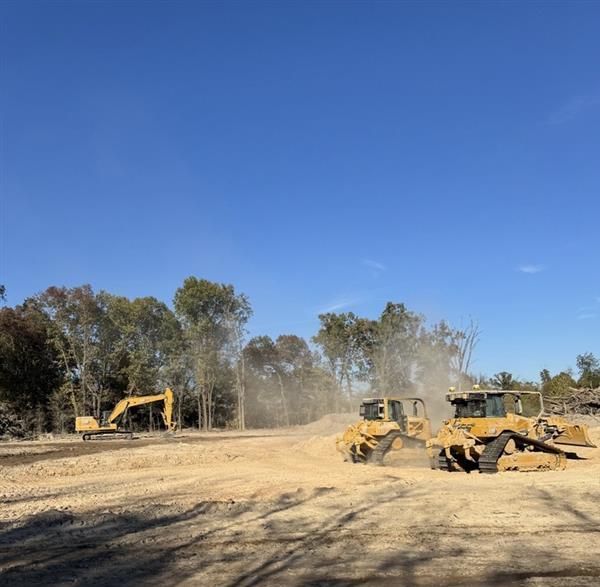 A group of construction vehicles are working on a dirt road.