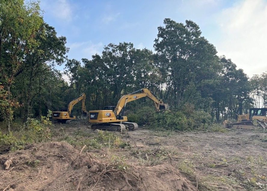 A couple of excavators are sitting in a field with trees in the background.