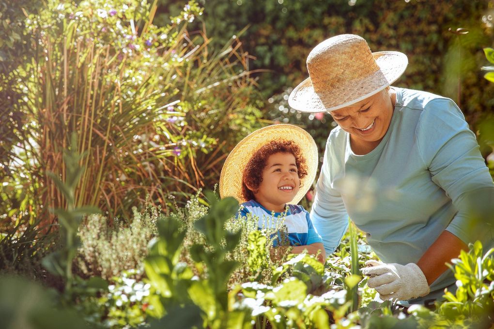 Woman and child in straw hats tending a garden, smiling in the sunlight.