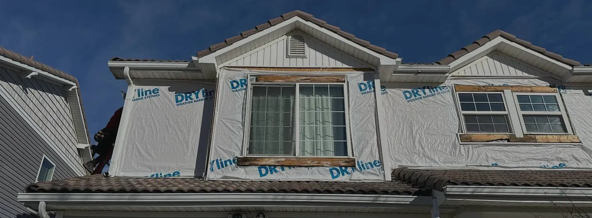 Row of townhouses under construction with white siding and gray roofs. Windows are covered with protective wrap.