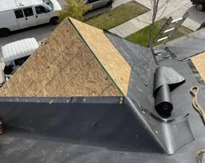 Rooftop under construction with plywood on one side and black underlayment on the other.  A roll of the underlayment is also visible.