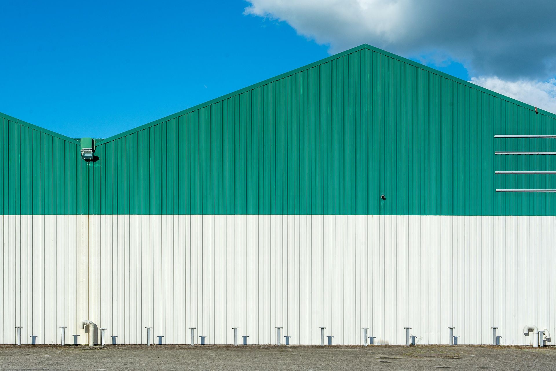 Green and white corrugated metal building against a bright blue sky with clouds.