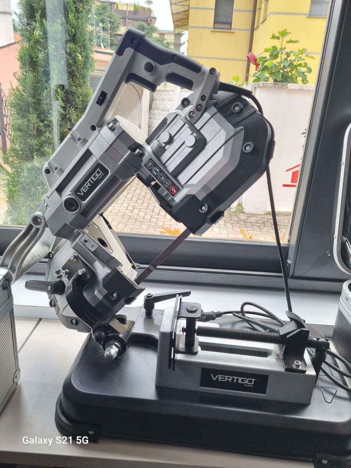 Una sega a nastro metallica su una base, posizionata vicino a una finestra. La sega è nera e argento, angolata e collegata alla presa di corrente.