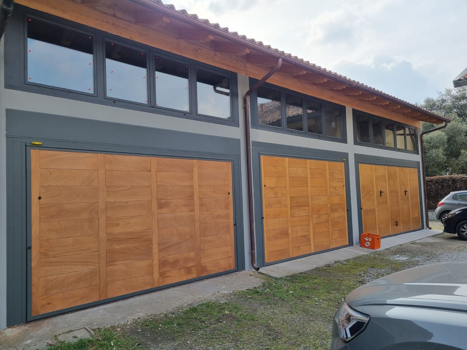 Tre porte da garage in legno sotto un edificio con pareti e finestre grigie.