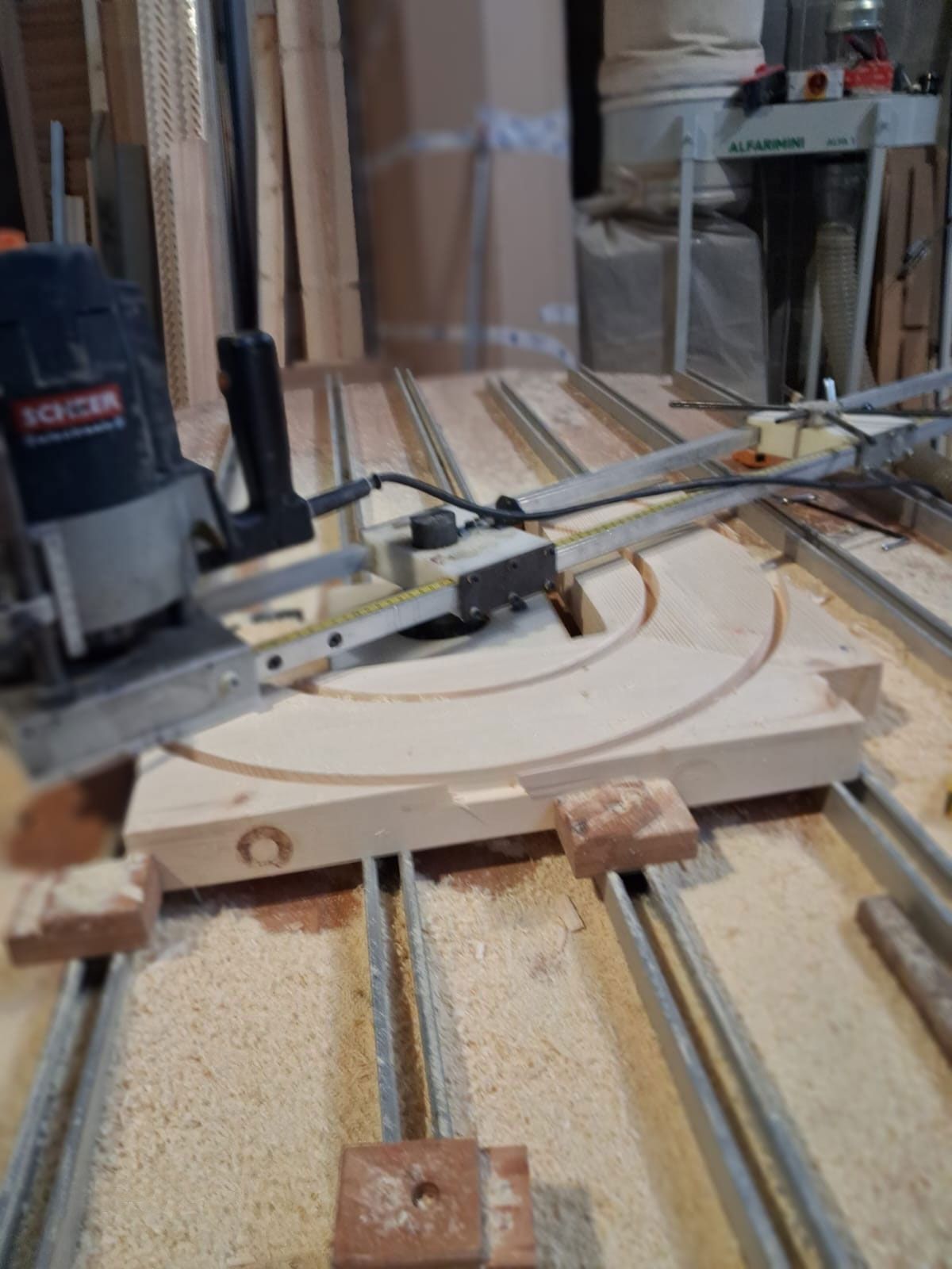 Fresatrice che taglia un arco nel legno su un banco da lavoro con binari metallici e segatura.