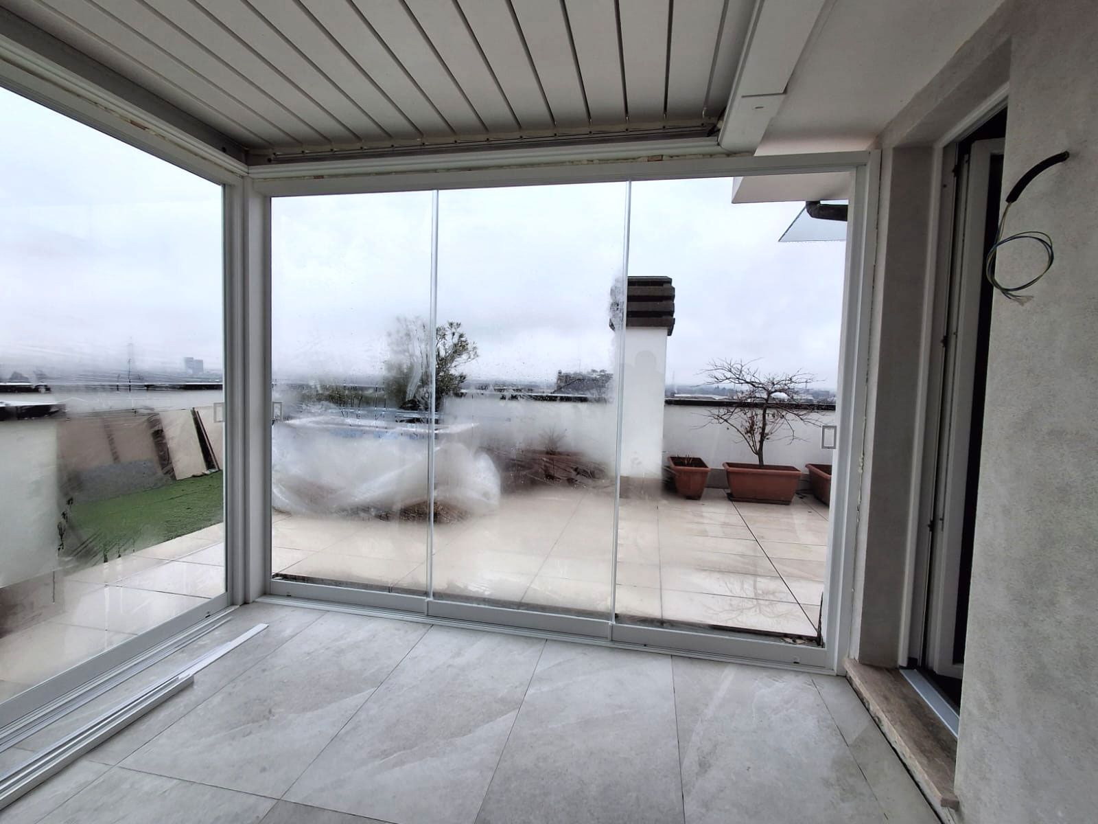 Patio sul tetto con vetrate e porte scorrevoli in vetro, con vista sulla città in una giornata nuvolosa.