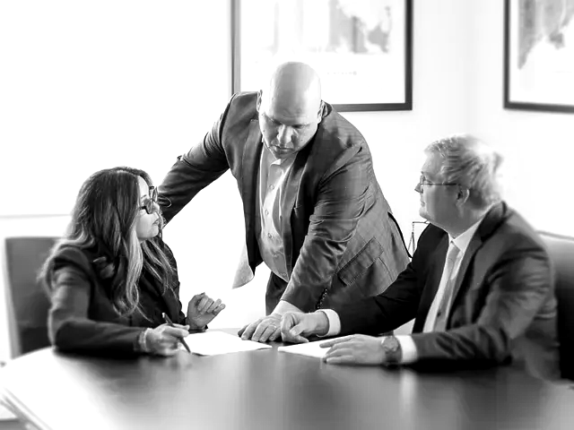 Three business people discussing documents around a table in a bright office