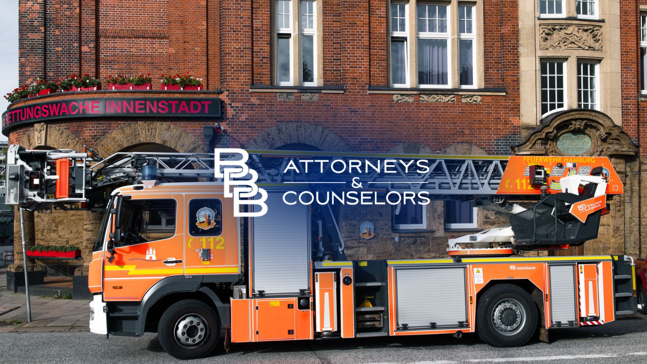 Orange utility truck with elevated crane parked in front of brick building with attorney sign