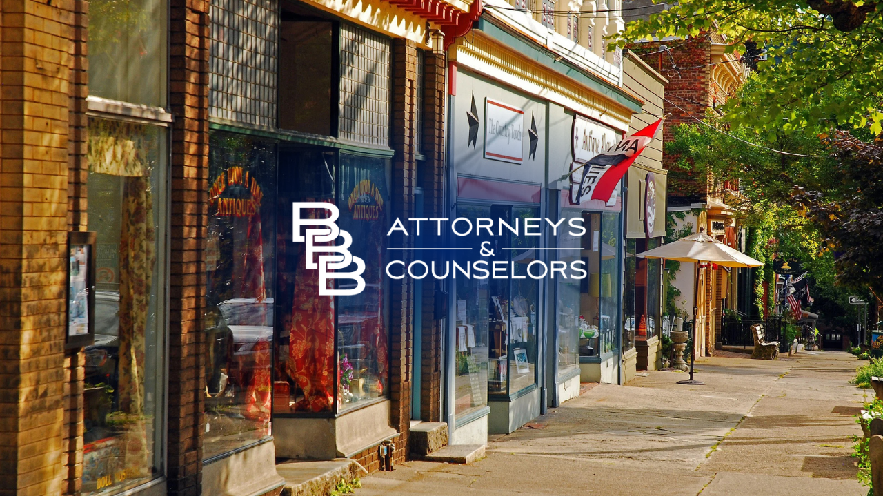Brick storefronts on a sunny sidewalk with an “Attorney’s Counselors” sign in the window