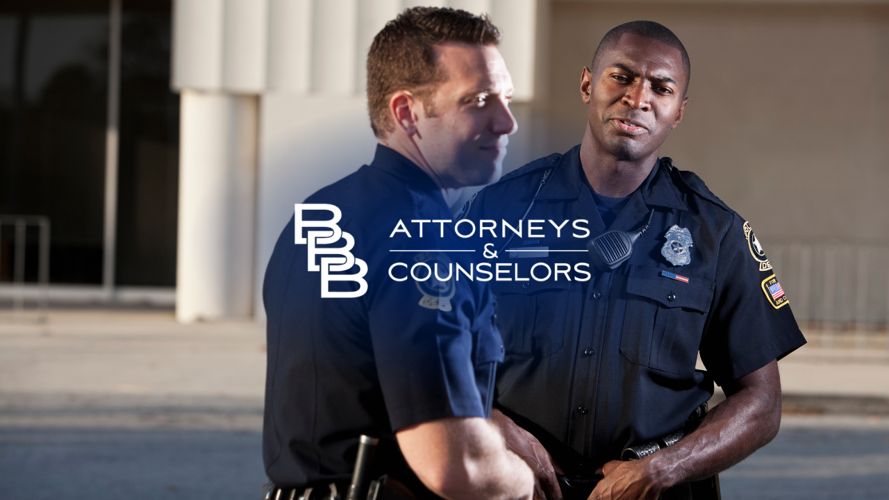 Two police officers standing outside a building, with one wearing a navy uniform and badge.