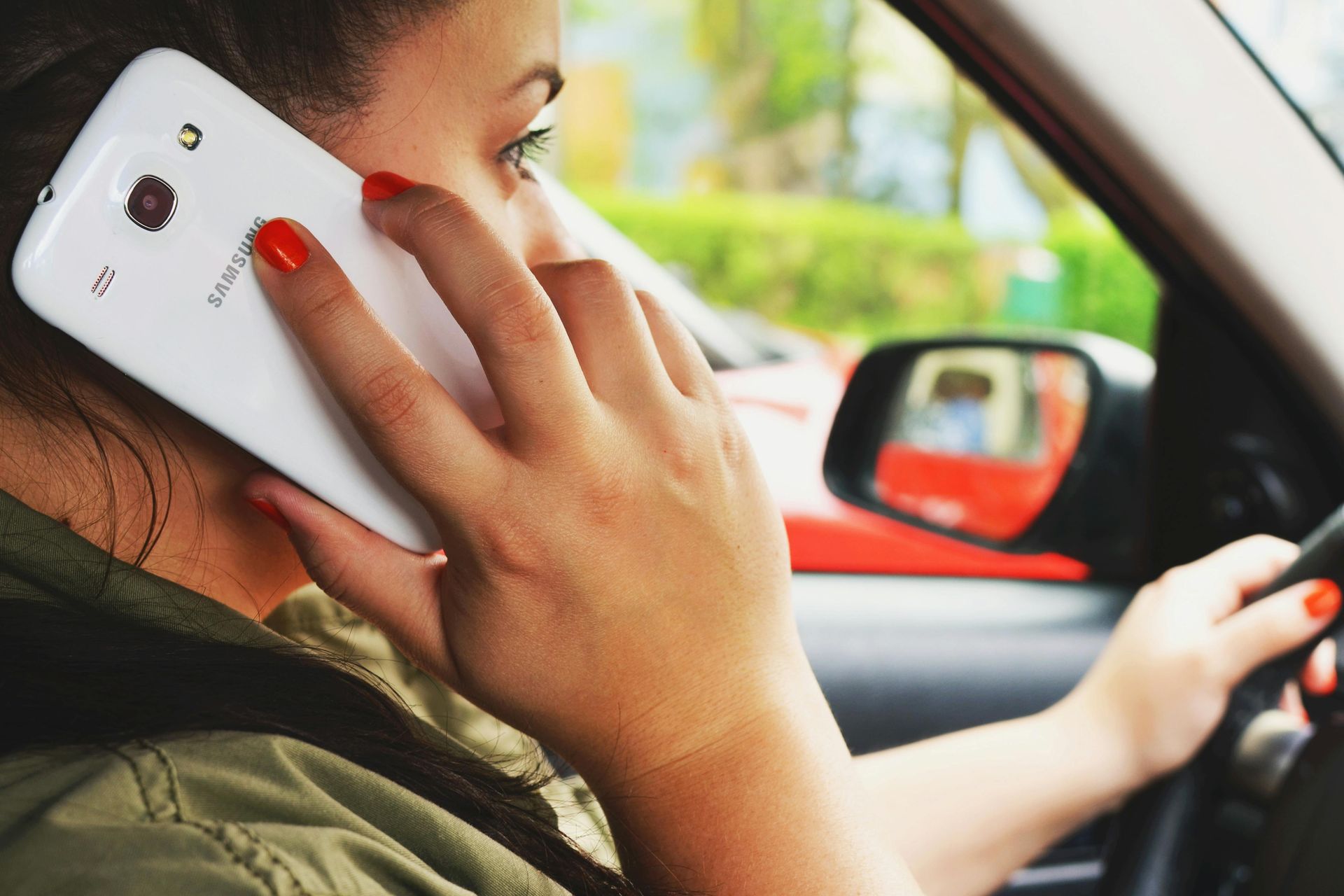 Woman driving a car while talking on a white smartphone held to her ear