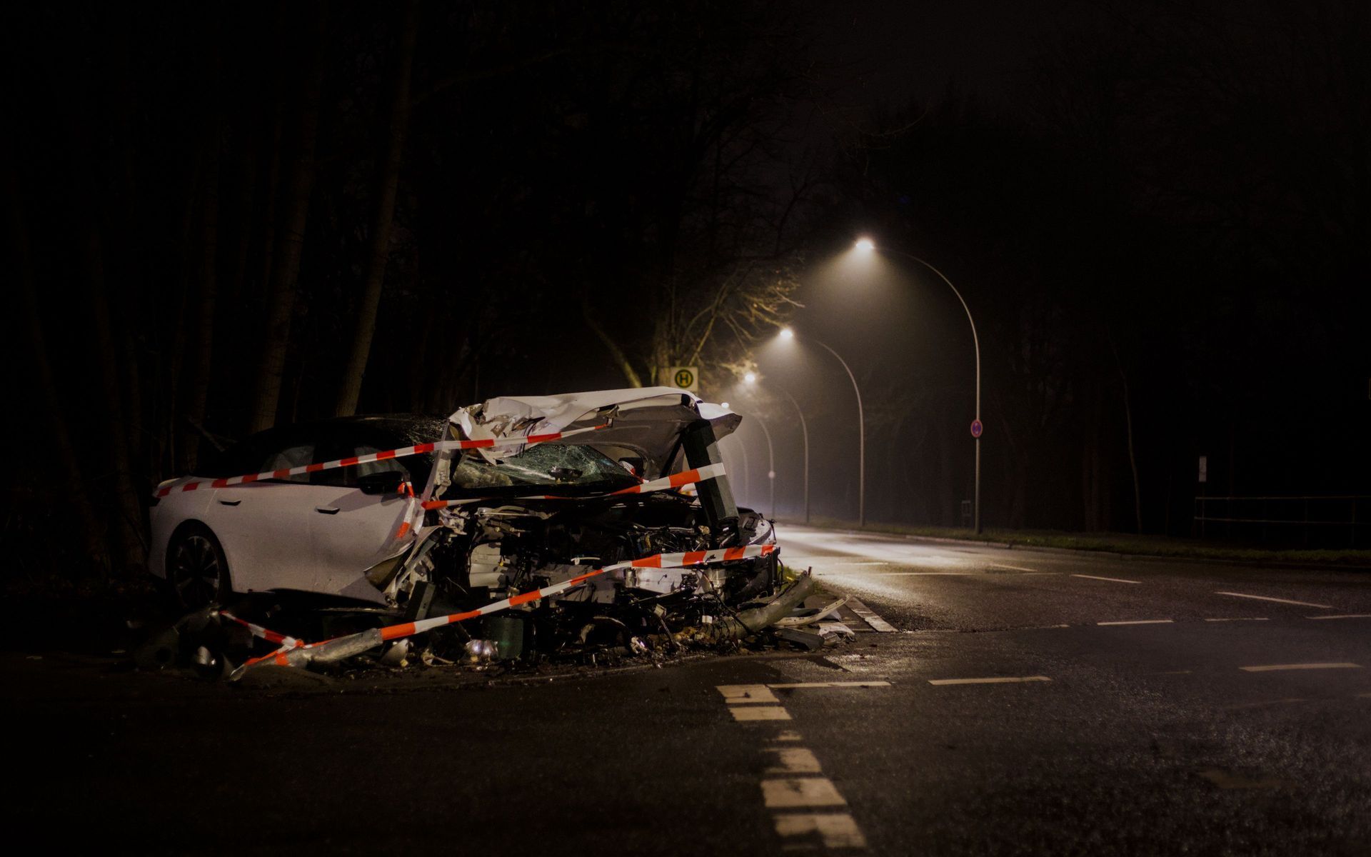 Severe nighttime car crash with a wrecked white SUV on a dark, wet road under streetlights