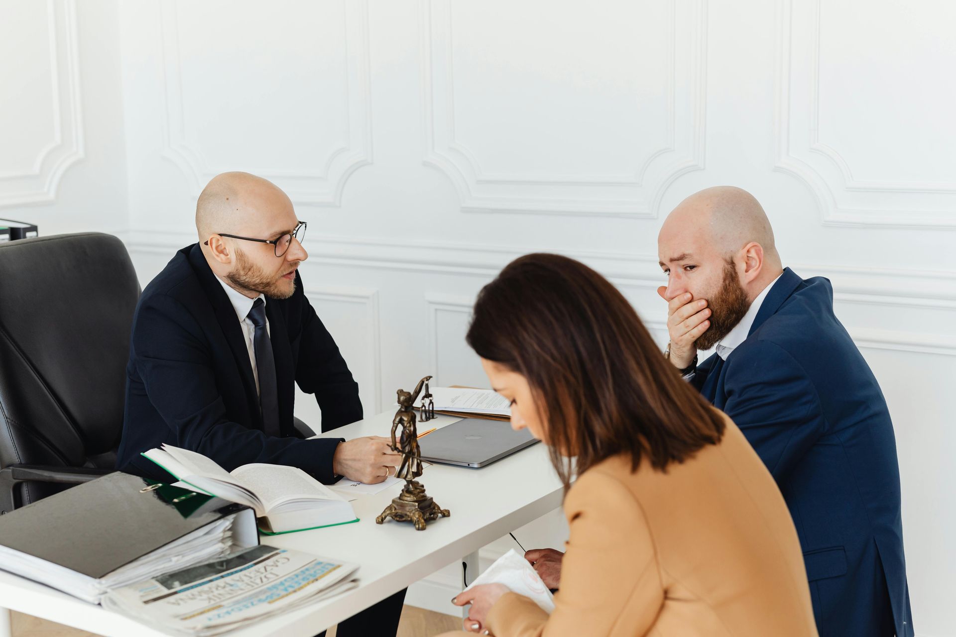 Three coworkers in a meeting around a desk with papers, a laptop, and a small statue.